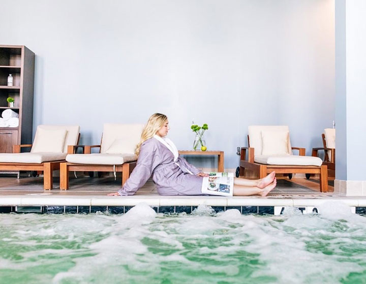 woman in robe lounges on the deck next to the indoor pool at Kimpton Overland Hotel